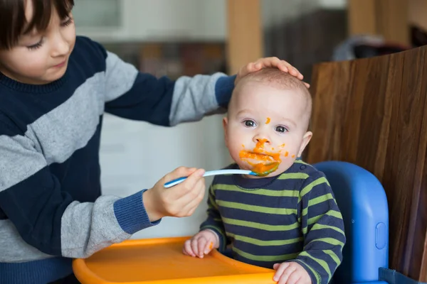 귀여운 유치원 아이, 으깬된 야채와 그의 동생을 먹이 — 스톡 사진