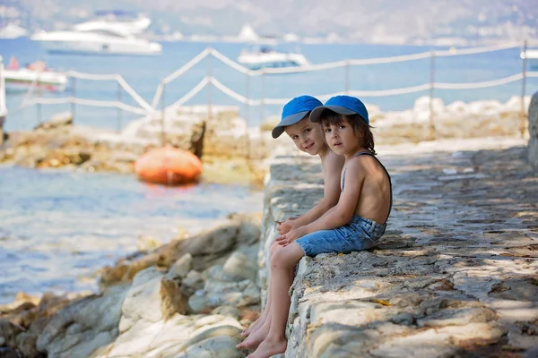 Due figli, fratelli maschi, seduti su un pontile sulla sponda mediterranea — Foto Stock