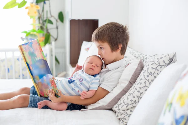 Dulce niño preescolar, leyendo un libro a su hermano recién nacido, sentado — Foto de Stock