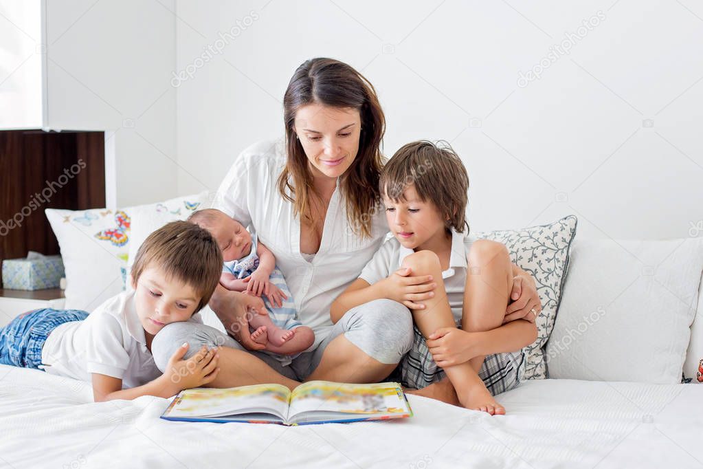 Young mother, read a book to her three children, boys, in the be