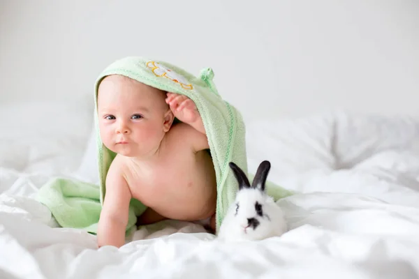 Niedlicher kleiner Junge mit kleinem Kaninchen im Bett nach dem Bad, Baby — Stockfoto