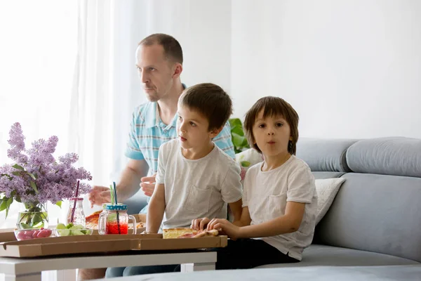 Отец и два его мальчика, дети, едят пиццу дома и ватк — стоковое фото