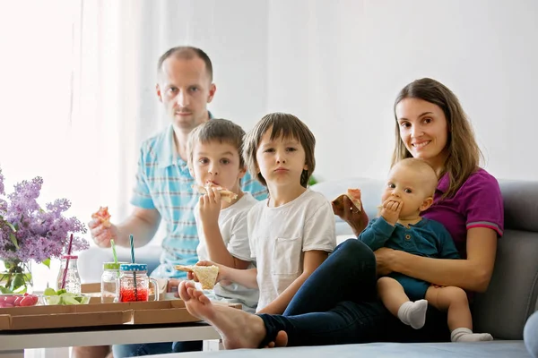 Молодая семья с тремя детьми ест пиццу дома — стоковое фото