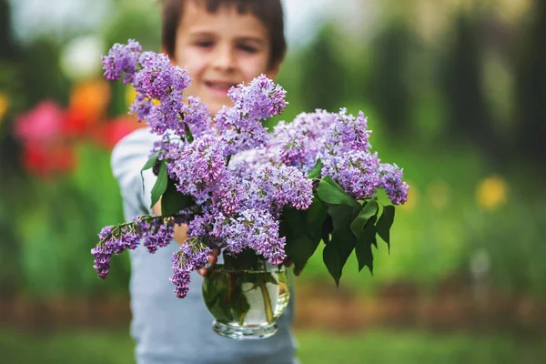 Dolce bambino, ragazzo, vaso con fiori lilla in giardino, pre — Foto Stock