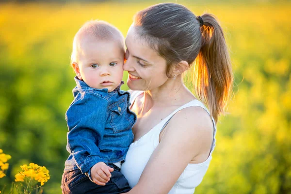 Young mother holding up her todller son in canola field — Stock Photo, Image