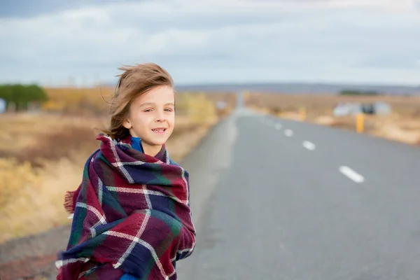 Güzel çocuk, çok rüzgarlı bir günde yolda duruyor, sarılmış. — Stok fotoğraf