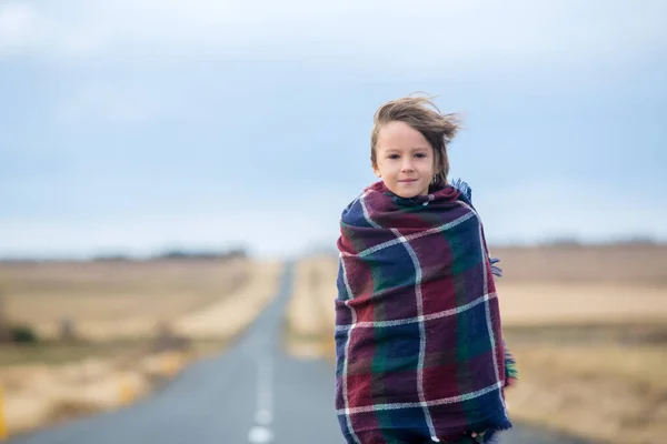 Schönes Kind, das an einem sehr windigen Tag auf einer Straße steht, eingewickelt — Stockfoto