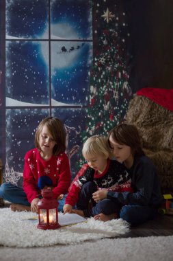 Üç çocuk, erkek kardeşler, Noel gecesi kitap okuyorlar.
