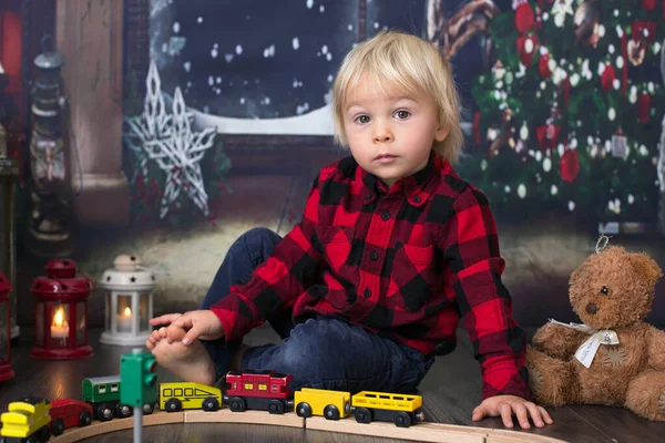 Menino criança doce, brincando com trem de madeira em casa à noite em — Fotografia de Stock