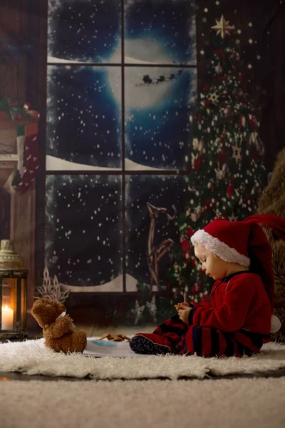 Dulce niño, leyendo libro en casa por la noche en Navidad —  Fotos de Stock