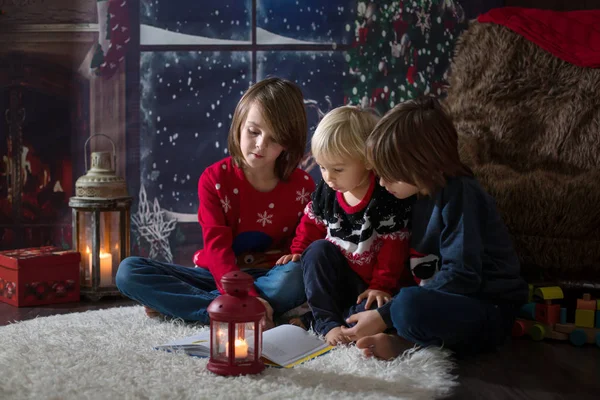 Tres niños, hermanos, leyendo un libro en la noche de Navidad —  Fotos de Stock