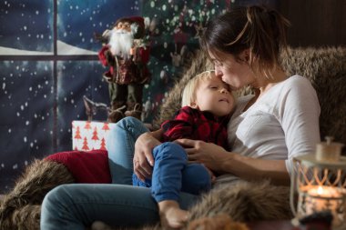 Güzel genç anne, küçük oğluna sarılıyor, rahat bir şekilde oturuyor.