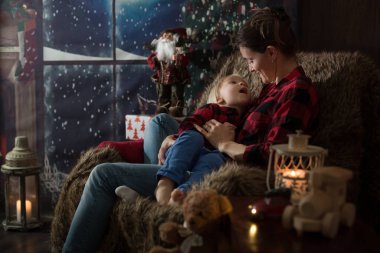 Güzel genç anne, küçük oğluna sarılıyor, rahat bir şekilde oturuyor.