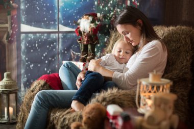 Güzel genç anne, küçük oğluna sarılıyor, rahat bir şekilde oturuyor.