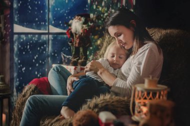 Güzel genç anne, küçük oğluna sarılıyor, rahat bir şekilde oturuyor.
