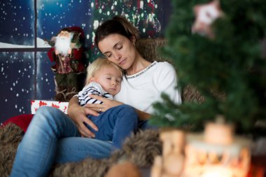 Güzel genç anne, küçük oğluna sarılıyor, rahat bir şekilde oturuyor.