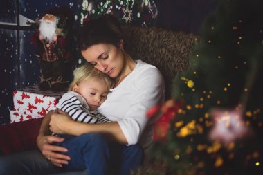 Güzel genç anne, küçük oğluna sarılıyor, rahat bir şekilde oturuyor.