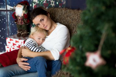 Güzel genç anne, küçük oğluna sarılıyor, rahat bir şekilde oturuyor.