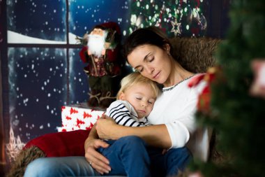 Güzel genç anne, küçük oğluna sarılıyor, rahat bir şekilde oturuyor.