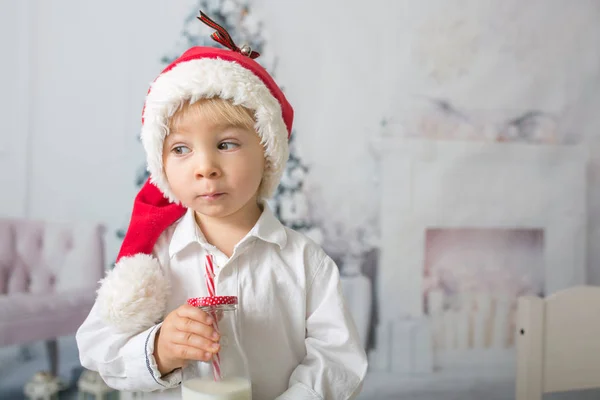 Beautiful toddler boy with red santa hat, holding bottle with mi — Stockfoto