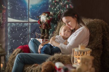 Güzel genç anne, küçük oğluna sarılıyor, rahat bir şekilde oturuyor.