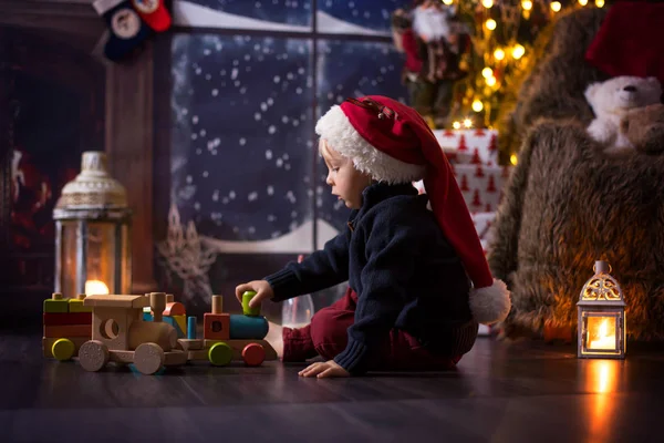 Sweet toddler boy, playing with wooden train at home at night on — Stock Photo, Image