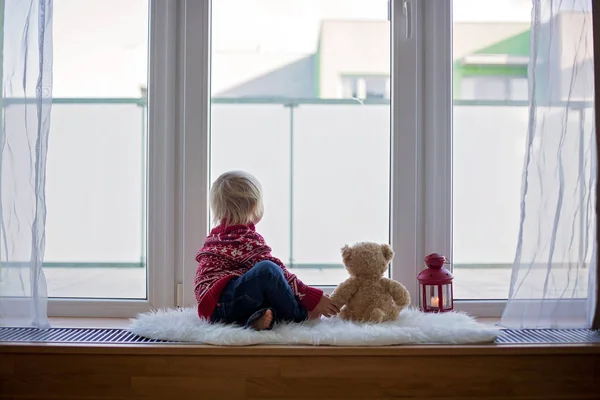 Zoet blond kind, jongen, zitten op venster schild met teddy bea — Stockfoto