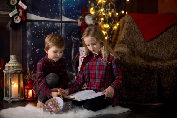 Menina pré-escolar bonito e menino, sentado ao lado da árvore de Natal, ope — Fotografia de Stock