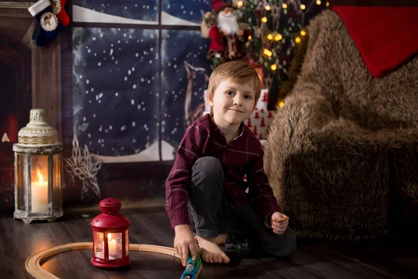 Lindo niño preescolar, sentado al lado del árbol de Navidad, jugando con —  Fotos de Stock
