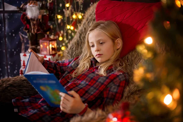 Aranyos óvodás lány ül körül karácsonyfa hangulatos szék, — Stock Fotó