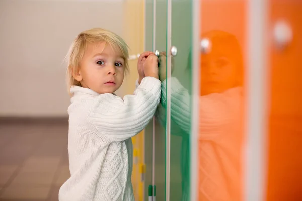 Lief blond peuter jongen staan in de voorkant van een kluisjes in kinde — Stockfoto