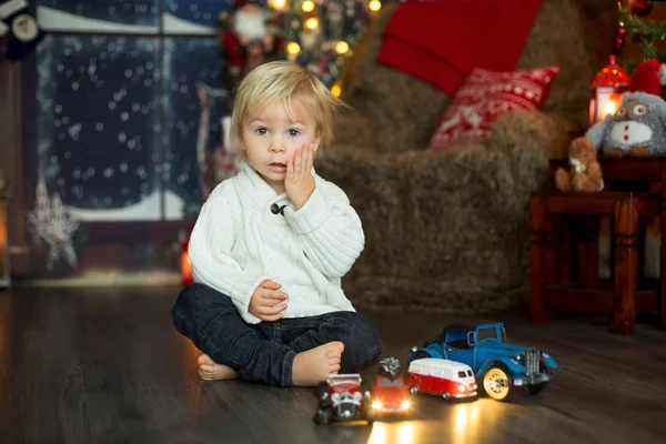 Lindo niño pequeño, sentado alrededor de muchos juguetes de coche en el suelo, pla —  Fotos de Stock