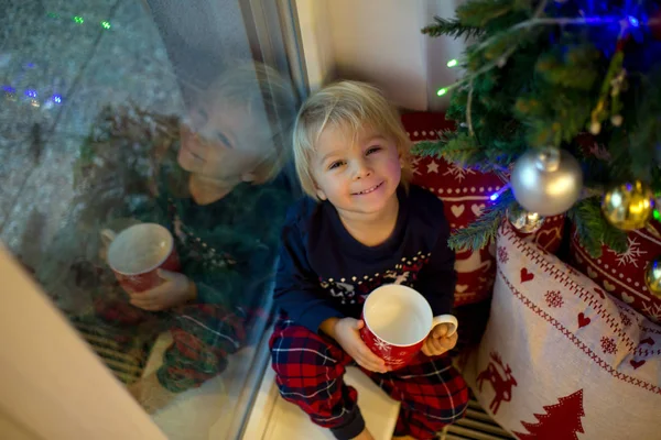 Lief peuter jongen in kerst pyjama, zitten op venster sluiten t — Stockfoto