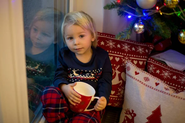 Menino doce criança no pijama de Natal, sentado na janela perto t — Fotografia de Stock