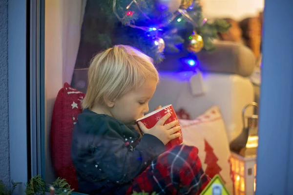 可爱的小孩，穿着圣诞睡衣，坐在窗户上，紧闭着 — 图库照片