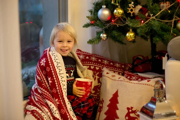 Noel pijamalı tatlı çocuk, pencerenin kenarında oturuyor. — Stok fotoğraf