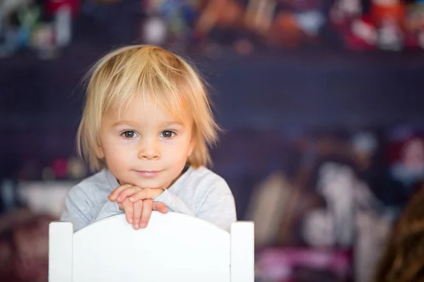 Schöner blonder kleiner Junge, der auf einem Stuhl sitzt, mit Spielzeug spielt — Stockfoto