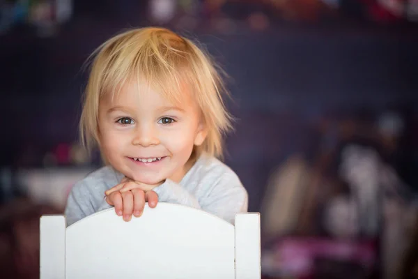 아름다운 금발의 사내 아이가 의자에 앉아 장난감을 가지고 놀고 있는 모습 — 스톡 사진