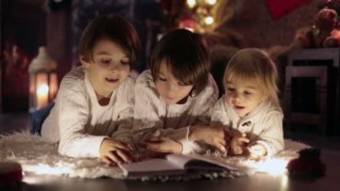 Üç çocuk, erkek kardeşler, Noel akşamı evde kitap okuyor, yerde yatıyorlar.