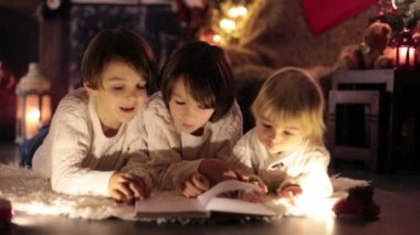 Üç çocuk, erkek kardeşler, Noel akşamı evde kitap okuyor, yerde yatıyorlar.