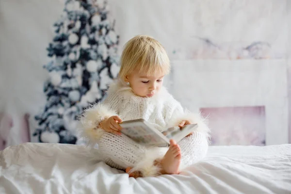 Блондинка малюк, хлопчик, читає книгу вдома, сидить у ліжку — стокове фото