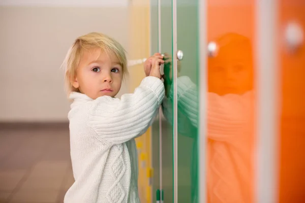 Sweet blonde toddler boy standing in front of a lockers in kinde — ストック写真