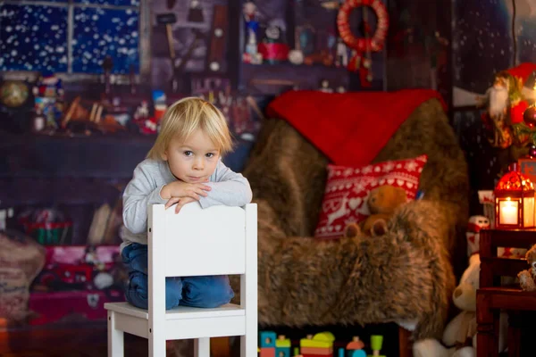 Schöner blonder kleiner Junge, der auf einem Stuhl sitzt, mit Spielzeug spielt — Stockfoto