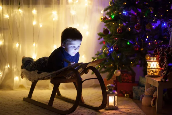 Niedliche entzückende Junge liest ein Buch vor dem Weihnachtsbaum, — Stockfoto