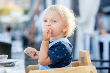 Sevimli yürümeye başlayan çocuk, bir restoranda yüksek sandalyede oturan, yemek 