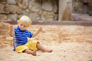Küçük çocuk, oyun alanında kum havuzunda kumla oynuyor.
