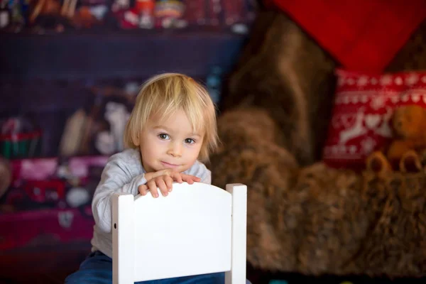 Schöner blonder kleiner Junge, der auf einem Stuhl sitzt, mit Spielzeug spielt — Stockfoto