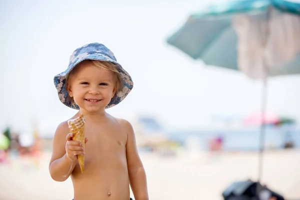 Słodki blond chłopiec maluch, eaiting lody na plaży — Zdjęcie stockowe