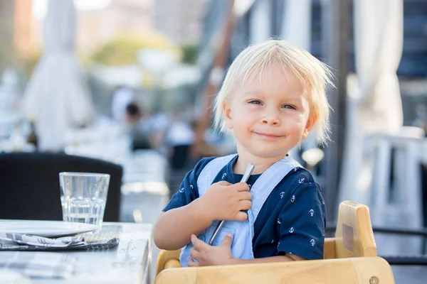 Lindo niño pequeño, sentado en la silla alta en un restaurante, drinkin —  Fotos de Stock