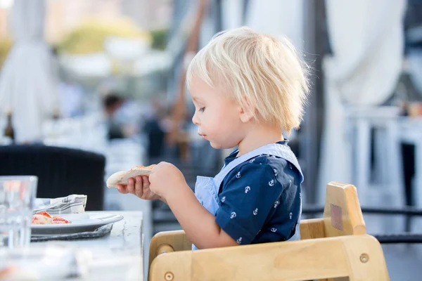 Niedliche Kleinkind Junge, sitzt im Hochstuhl in einem Restaurant, essen — Stockfoto